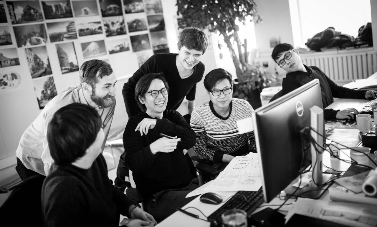 Tomasz laughing with teammates around a monitor at MAD